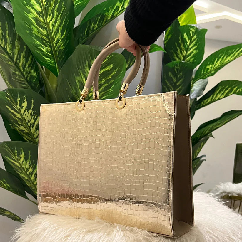 Gold handbag with brand logo on a fluffy white surface with green plants in the background