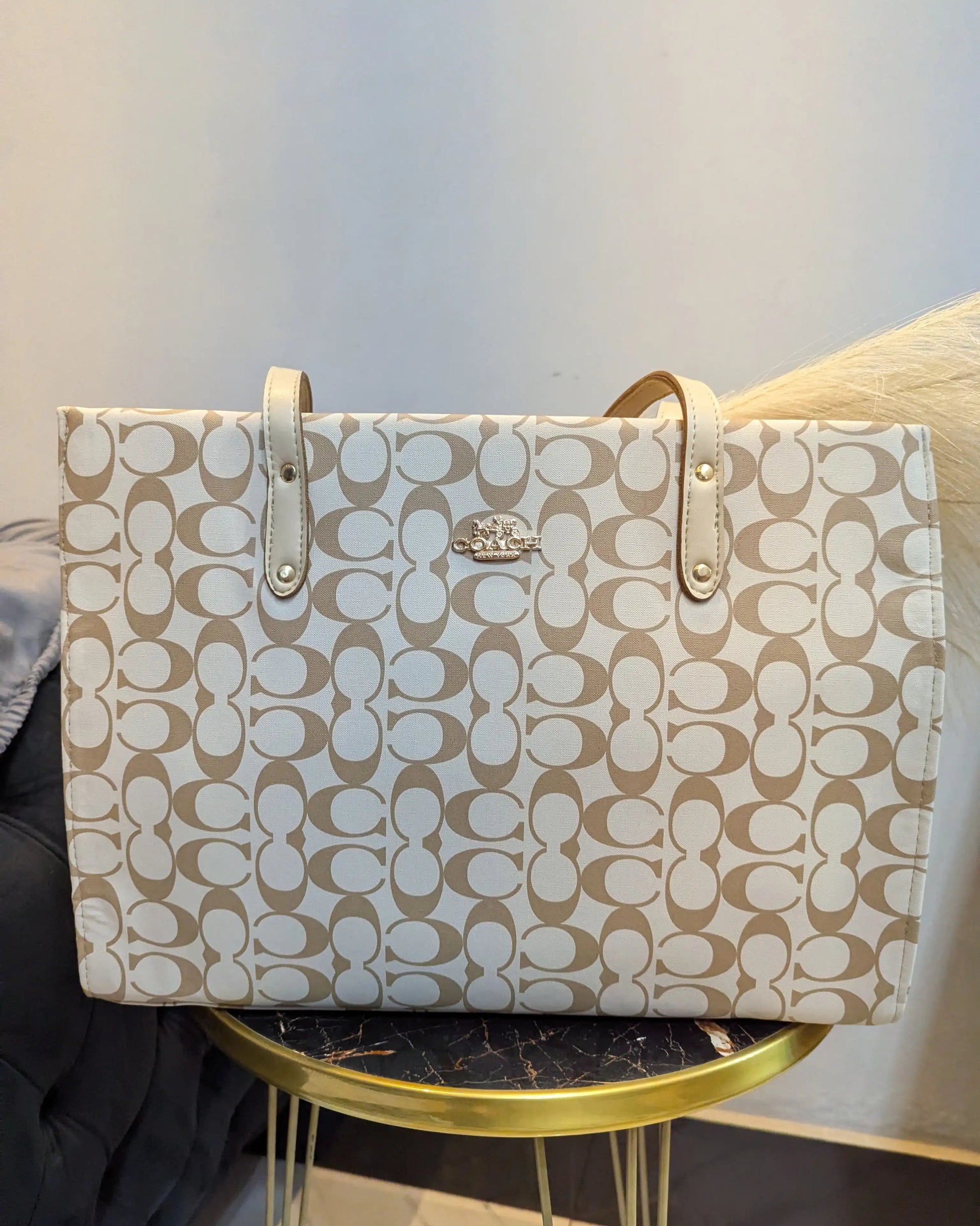 Beige handbag with a pattern on a gold stand against a light background