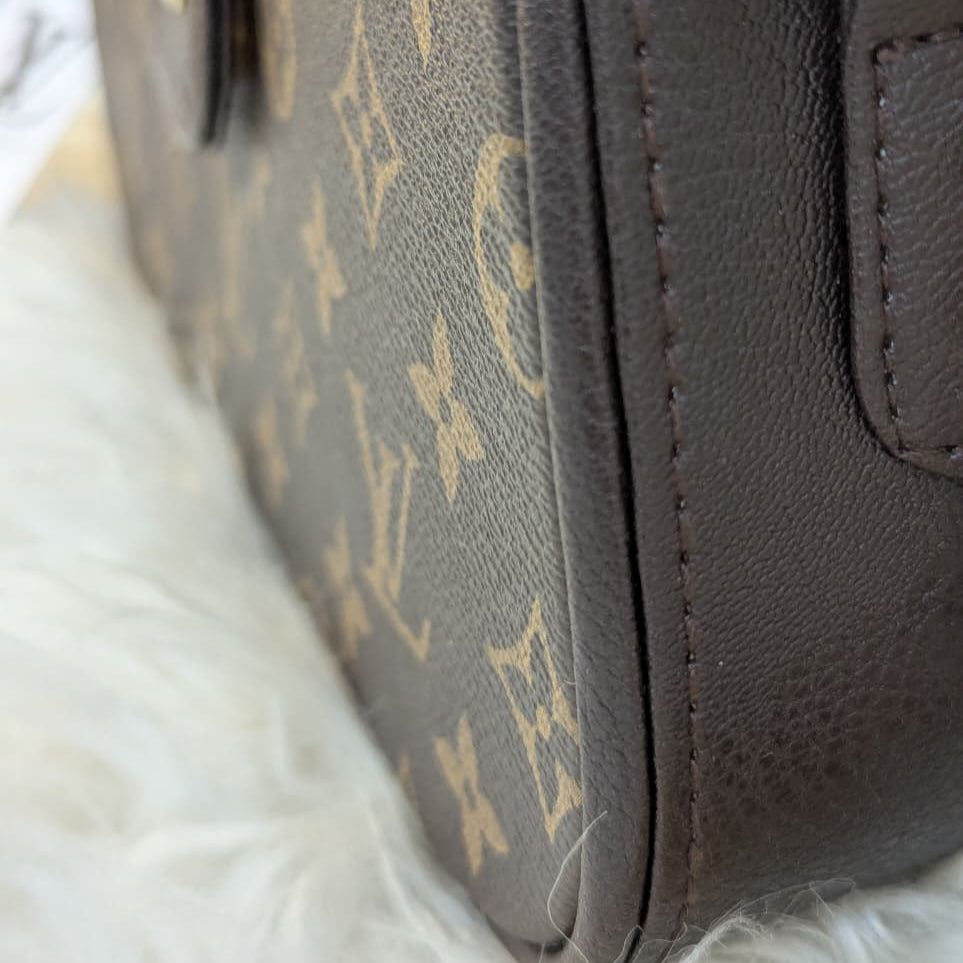 Close-up of a brown leather handbag with a visible brand logo on a white fur surface.